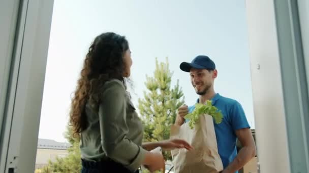 Νεαρή γυναίκα που παίρνει χάρτινη σακούλα με οργανικά τρόφιμα από deliveryman και πληρώνει με smartphone — Αρχείο Βίντεο