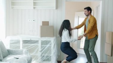Neşeli erkek ve kadın dans ediyor. Yeni evde müzik dinliyorlar. Etrafında kutular var.