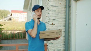 Üniformalı adam pizza dağıtıyor cep telefonuyla konuşuyor sonra da mutlu kıza kutular veriyor.