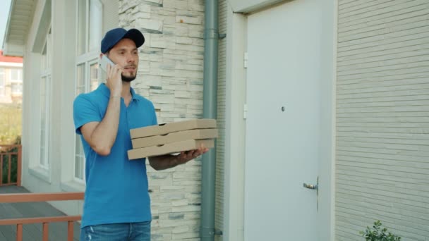 Доставка людина розмовляє на мобільному телефоні, а потім дає коробки з їжею клієнту, що стоїть на вулиці — стокове відео