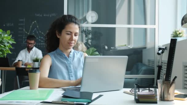 Employée utilisant un ordinateur portable tapant assis au bureau dans un bureau en verre partagé — Video