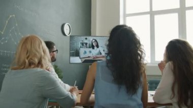 İş adamlarından oluşan bir grup kadın meslektaşlarıyla görüntülü konuşma yapıyor ve çalışma masasında otururken görüntülere bakıyor.