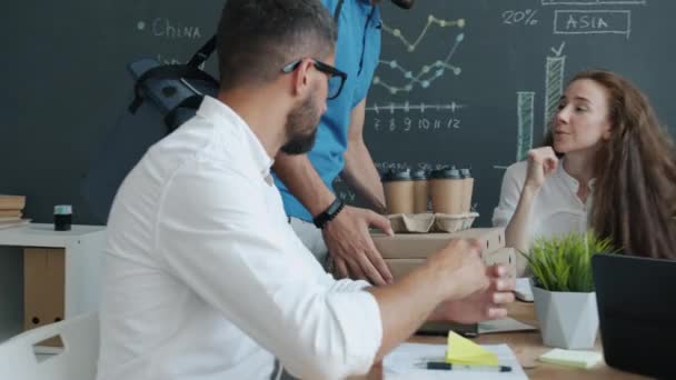 El repartidor lleva comida y bebida a los trabajadores de la oficina que hacen clic en las tazas de café durante el almuerzo — Vídeos de Stock