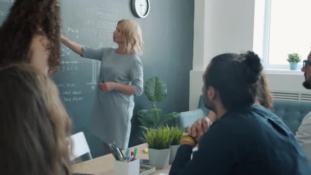 Confident business lady speaking to group of colleagues making presentation with chalkboard in office — Stock Video