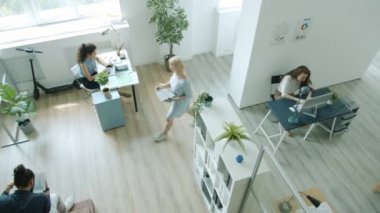 Yüksek açılı çalışanlar ofiste çalışan kadın ve erkeklerin bilgisayar kullanarak yürüdüklerini görürler.