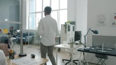 Genç adamın açık planlı ofiste iş arkadaşlarıyla buluşması ve sonra dijital kurul sunumunu izlemesi.