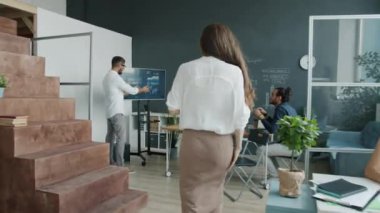 İş kadını iş arkadaşıyla sohbet ediyor sonra da etkileşimli kurul sunumunu izliyor ve takım arkadaşlarıyla fikir paylaşıyor.