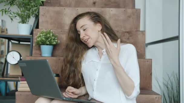 Радостная девушка сотрудник чата на видео-звонок с помощью ноутбука в офисе, в то время как люди идут на передний план — стоковое видео