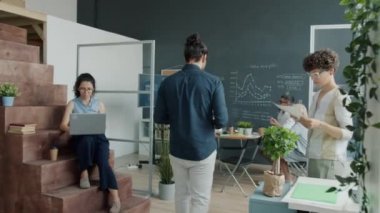 Karışık yarış bürosu çalışanı yürüyor sonra sunumu dinliyor ve işteki etkileşimli tahtaya bakıyor.