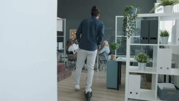 Homem árabe alegre montando scooter no escritório dando boas notícias aplaudindo e fazendo high-five com colegas de trabalho — Vídeo de Stock