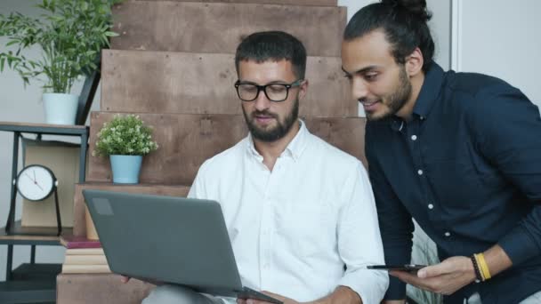Männliche Kollegen, die mit Laptop und Tablet arbeiten, tauschen sich im modernen kreativen Büro aus — Stockvideo