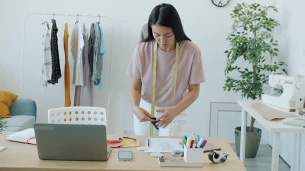 Framgångsrik asiatisk sömmerska välja material och färg för nya eleganta kläder som arbetar i studio ensam — Stockvideo