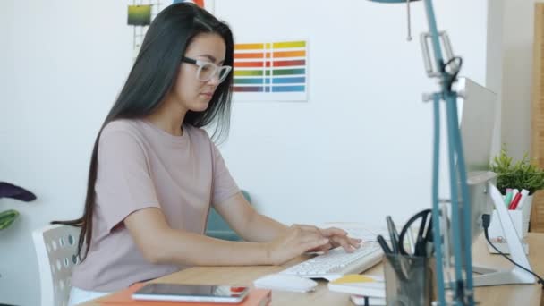 Portrét krásné asijské návrhářky pracující s počítačem psaní uvnitř v kanceláři — Stock video