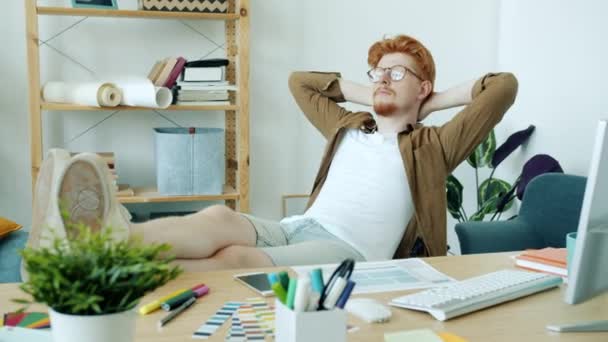 Joven freelancer sentado en sillón relajante pensando en el trabajo en el interior del apartamento — Vídeo de stock