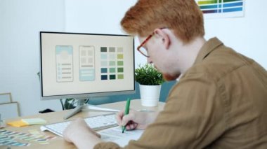 Ofiste çalışan bilgisayar ekranına bakarak mobil uygulama renklendirme yapan yaratıcı genç adam taslakları