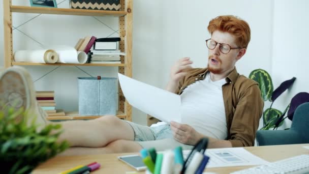 Diseñador cansado sentado en el lugar de trabajo en casa mirando la interfaz de la aplicación del teléfono inteligente pensando bostezo — Vídeo de stock