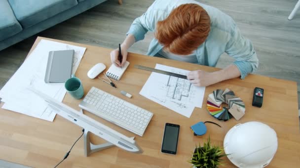 Mouvement lent de l'homme aux cheveux roux architecte travaillant avec le plan de construction à l'intérieur à la maison — Video