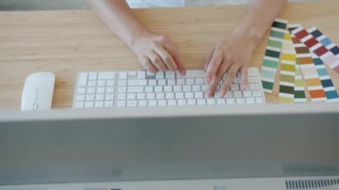 Ofisteki masalardaki renk paletlerine bakarak bilgisayar yazma kullanan profesyonel tasarımcının yüksek açılı görünümü