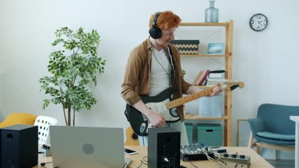 Медленный портрет веселого молодого человека, играющего на электрогитаре и веселящегося дома — стоковое видео