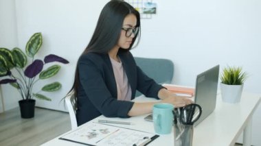 Bilgisayarla yazı yazan ve işyerinde kahve içen Asyalı güzel bir ofis çalışanının ağır çekimde