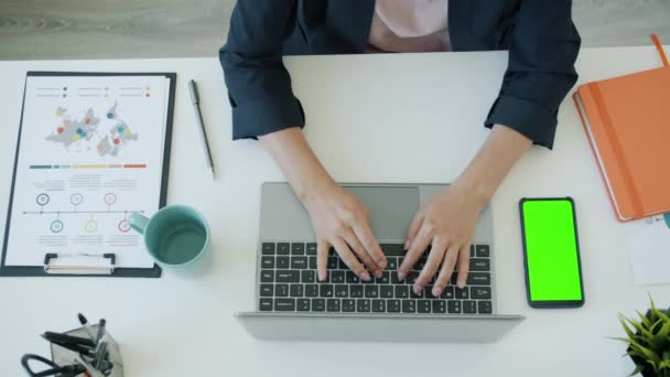 Крупный план рук бизнесвумен с помощью ноутбука, печатающего со смартфоном с зеленым экраном — стоковое видео