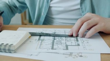 Mimarlar plan üzerinde çalışırken, erkek ellerinin cetvelle bina planlarını ölçerken yakın plan görüntüleri.