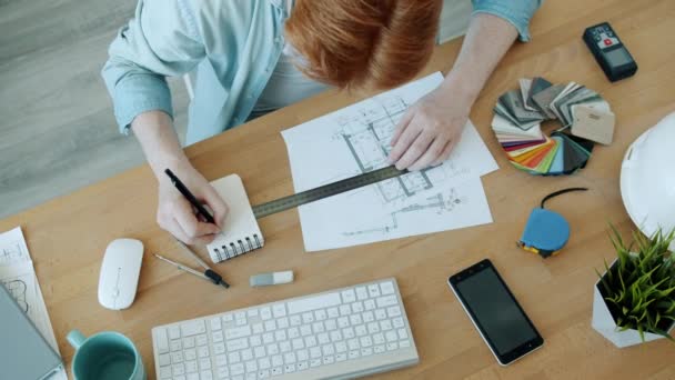 Vista de alto ângulo do arquiteto masculino trabalhando com o plano de construção fazendo medições e tomando notas — Vídeo de Stock