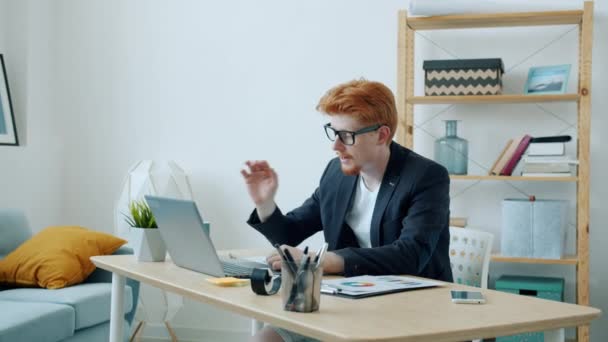 Långsam rörelse av ung affärsman gör online videosamtal med bärbar dator sedan lämnar rum i lägenhet — Stockvideo