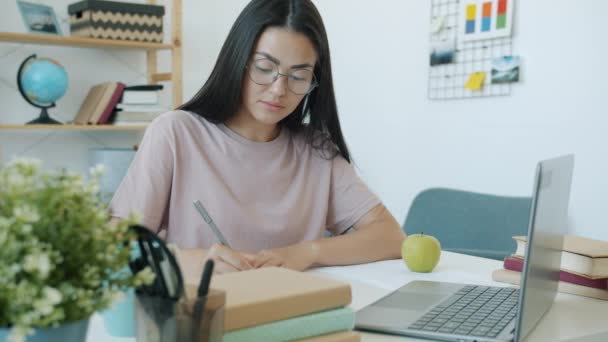 Όμορφο κορίτσι από την Ασία σπουδάζει στο σπίτι γράφοντας και κοιτάζοντας οθόνη laptop στο γραφείο — Αρχείο Βίντεο