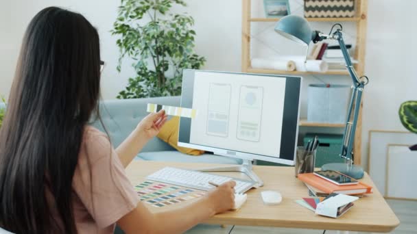 Tampilan belakang desainer aplikasi smartphone wanita memilih warna dengan melihat monitor pc yang bekerja di rumah — Stok Video