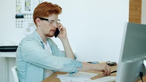 Retrato del arquitecto serio discutiendo el trabajo en el teléfono móvil y trabajando en el plano en la oficina — Vídeos de Stock