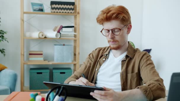 Cámara lenta de los jóvenes especialistas masculinos bosquejo en la pantalla de la tableta de trabajo en interiores en el apartamento — Vídeo de stock