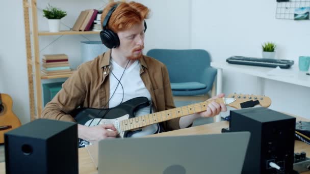 Movimento lento do jovem guitarrista tocando instrumento elétrico usando fones de ouvido e usando equipamentos em casa — Vídeo de Stock