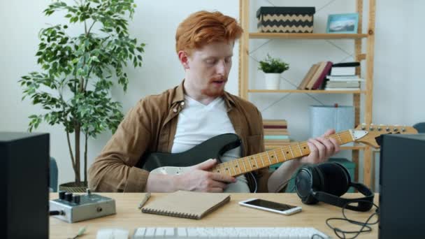 Retrato del guapo guitarrista hablando sosteniendo un instrumento musical durante una videollamada en línea en casa — Vídeos de Stock
