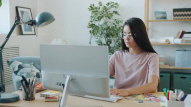 Genç Asyalı kadın uygulama tasarımcısı bilgisayar kullanıyor ve evdeki akıllı telefon ekran görüntülerine bakıyor