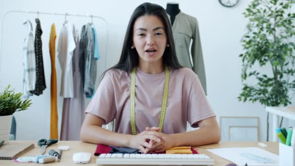 Retrato de hermosa diseñadora de moda asiática haciendo videollamada en línea hablando y saludando de la mano en el estudio — Vídeo de stock
