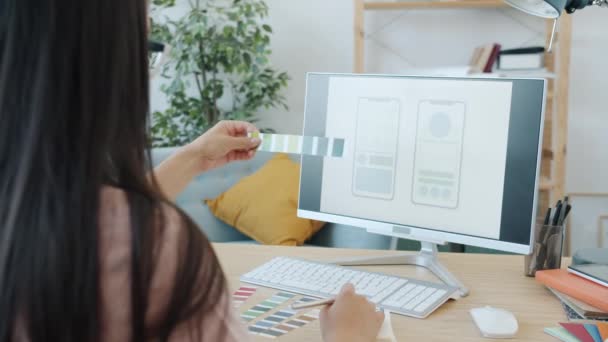 Специалистка-женщина разрабатывает интерфейс мобильного приложения, рассматривая экран компьютера с цветными палитрами, работающими дома — стоковое видео