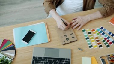 Erkek ellerinin kağıda logo tasarımı çizerken yavaş çekimde kapalı alanda dizüstü bilgisayar kullanması.