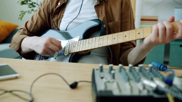 Медленное движение музыканта, играющего на электрогитаре и регулирующего оборудование, практикующегося в одиночку дома — стоковое видео