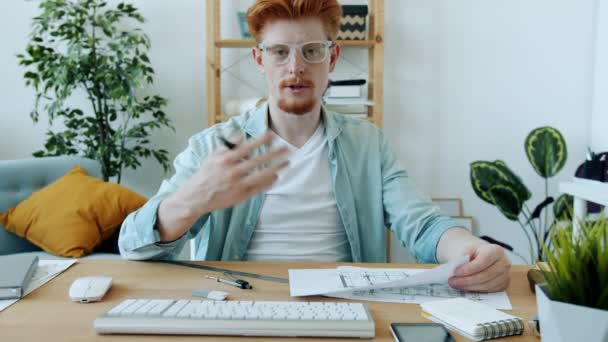 Arquitecto masculino serio hablando y apuntando al plano durante la videollamada en línea desde casa — Vídeos de Stock