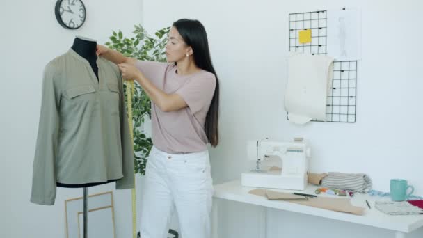 Seriöser asiatischer Modedesigner misst Kleidungsstück an Schneiderattrappe und beschäftigt sich mit kreativer Arbeit im Atelier — Stockvideo