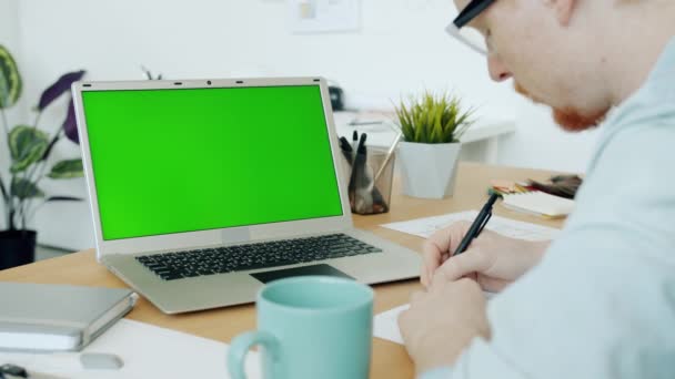 Αργή κίνηση του νεαρού αρχιτέκτονα που εργάζεται με τον υπολογιστή κοιτάζοντας το πράσινο chroma πληκτρολόγηση οθόνης κλειδί — Αρχείο Βίντεο