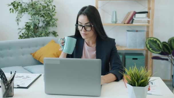 Långsam rörelse av kvinnliga asiatiska entreprenör med bärbar dator som arbetar hemifrån skriva dricka kaffe — Stockvideo