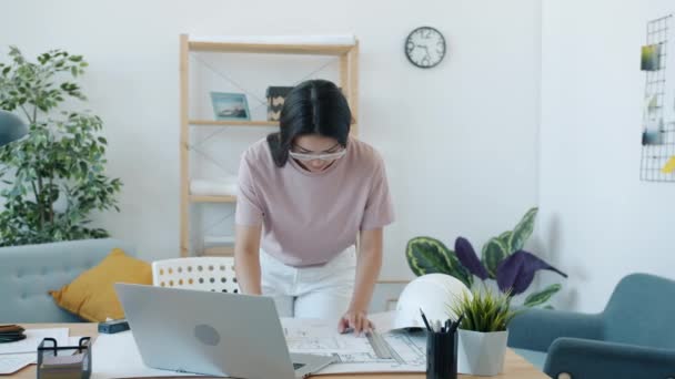 Young Asian woman architect working with blueprint making measurements alone at home — Stock Video
