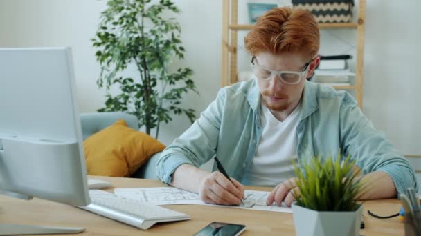 Bonito arquiteto homem ruiva-haired trabalhando em casa desenho plano e usando computador — Vídeo de Stock