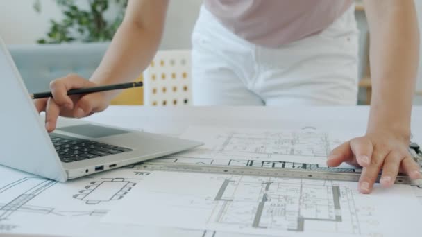Close-up slow motion of female architects hands working with blueprints and laptop indoors — Stock Video