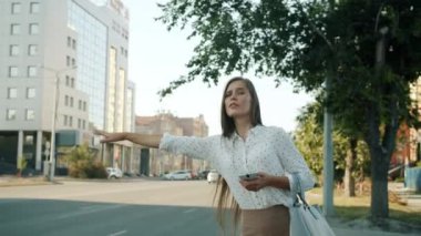 Şehir caddesinde acele içinde akıllı telefon ekranına bakan taksi çağıran kadının yavaş çekim portresi.
