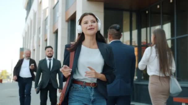 Feliz joven dama de negocios bailando al aire libre usando auriculares al aire libre en la calle ocupada — Vídeos de Stock