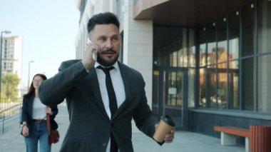Cep telefonuyla konuşan hırslı işadamlarının yavaş çekimde cam duvar ofis binasının yanında yürümeleri.
