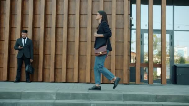 Vista lateral de la joven empresaria con estilo caminando por el moderno edificio de oficinas — Vídeos de Stock
